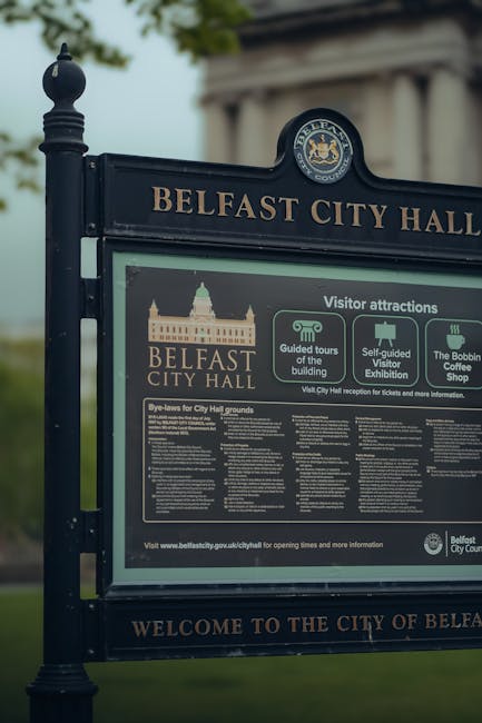 A close-up of an outdoor informational signboard at Belfast City Hall, featuring the city’s emblem at the top, with details about visitor attractions, guided tours, self-guided exhibitions, and the