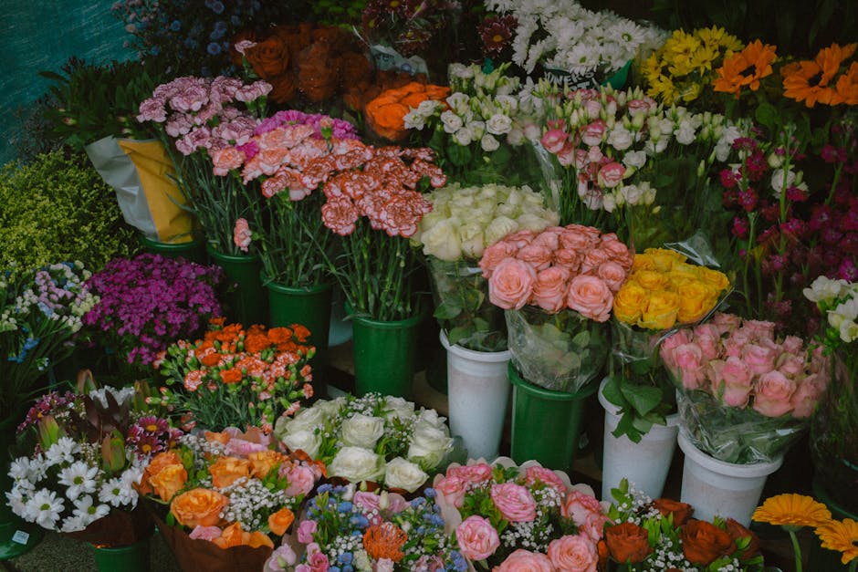 A display of various fresh floral bouquets and individual flower bunches at a flower shop, featuring roses in shades of pink, white, and yellow, as well as carnations, chrysanthemums, and other blooms