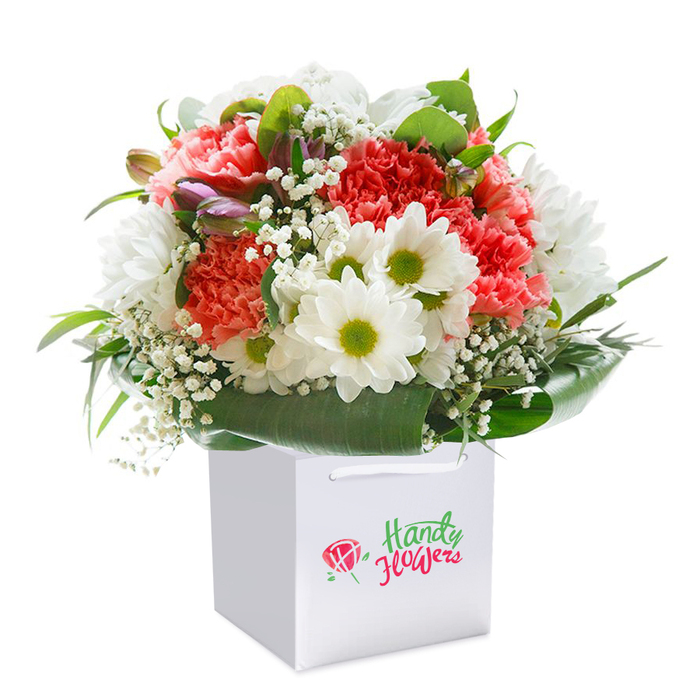 In this refined bouquet, an elegant symphony of color and texture is brought to life by Whetstone's skilled floral artisans. Picture lush coral and peach carnations, their frilly petals layered with intricate, feathery detail that evokes the gentle freshness of summer along Russell Lane. Juxtaposed with these are brilliant white daisies, each surrounded by vibrant lime-green centers that create a lively, uplifting presence throughout the arrangement. Wisps of dainty white baby's breath are artfully scattered, imparting a hint of airiness and softness, while the inclusion of purple-tinged, unopened flower buds lends dimension and a sense of natural unfolding. The flowers are enveloped within a collar of shiny, deep green leaves, forming a rich, protective cradle that enhances the bouquet's rounded silhouette. Housed inside a crisp, square white gift bag with robust ribbon handles, the bouquet appears freshly picked-perfect for gifting to friends in Whetstone or as a gracious offering for local occasions. The photograph's flawless white background ensures every shade and contour stands out, from the corals to the deep greens, reflecting the bouquet's premium quality and meticulous preparation. The overall effect is one of abundance and grace, a ready-to-deliver gift evocative of celebration and personal touch throughout the neighbourhood.